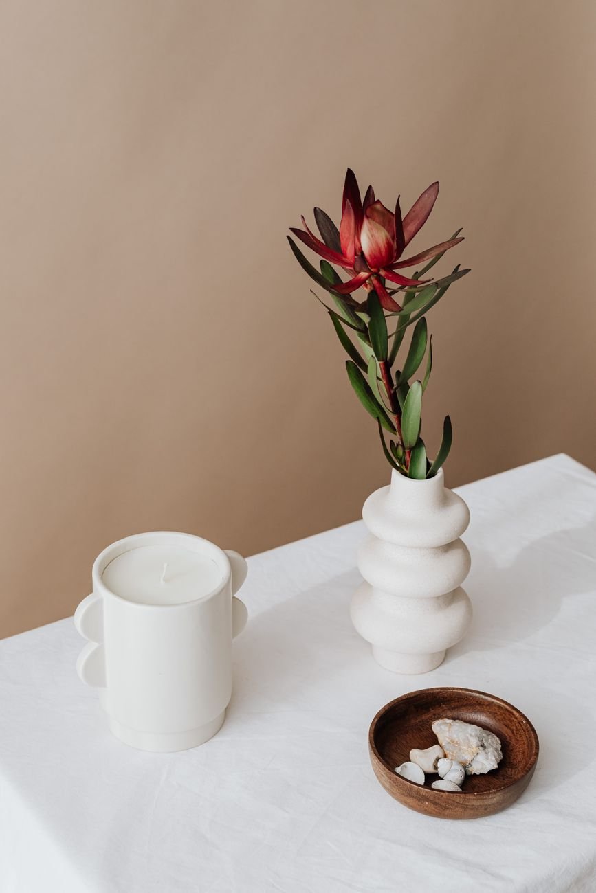 Minimalist setup with a white vase beside a candle and decorative stones.